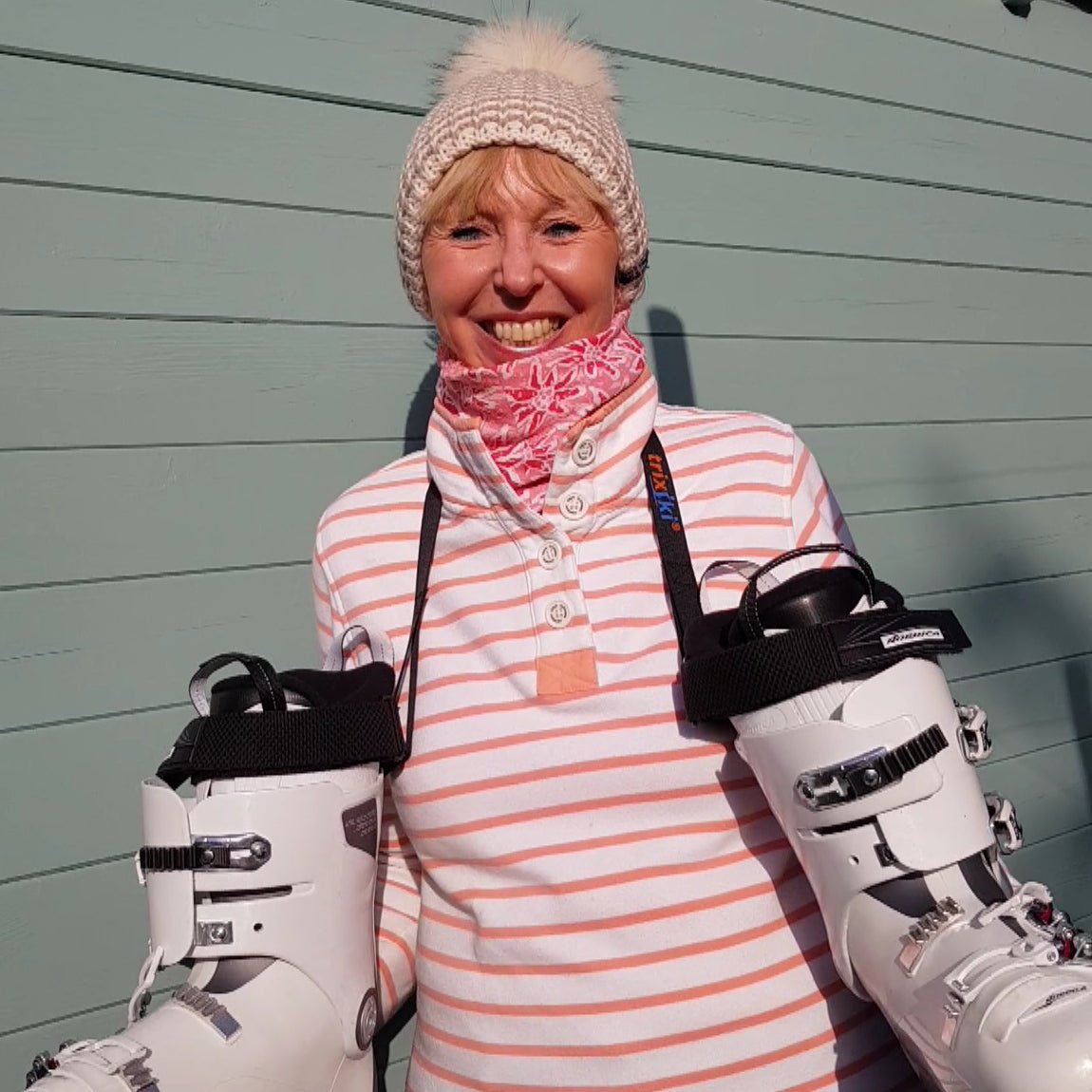 Happy skier using a bootstrap to carry ski boots round her neck