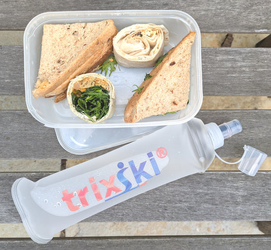 Picnic lunch container with sandwich and snacks, featuring a trixski silicone water bottle.