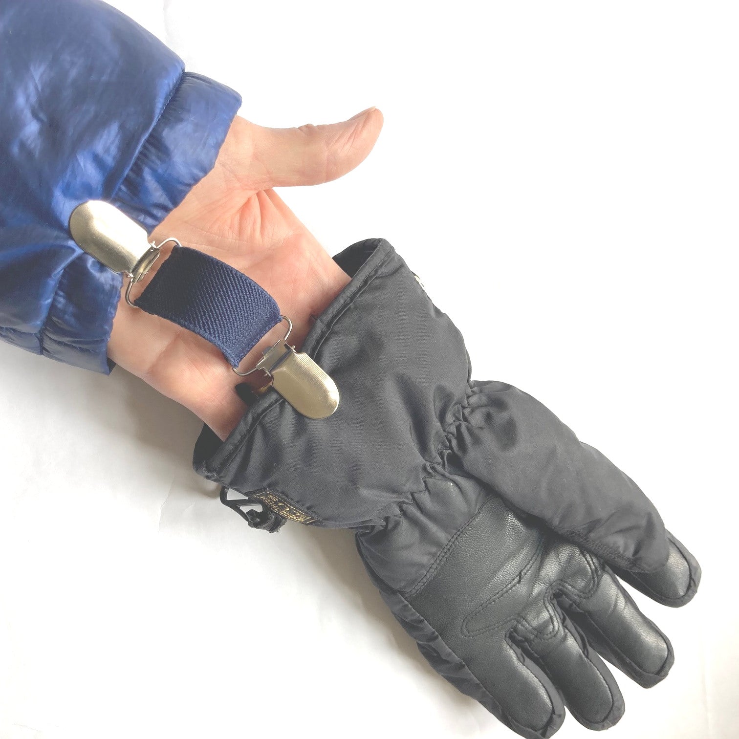 Close up of a navy Clip2Cuff attached to a cuff at one end and a glove at the other end of the elastic strap