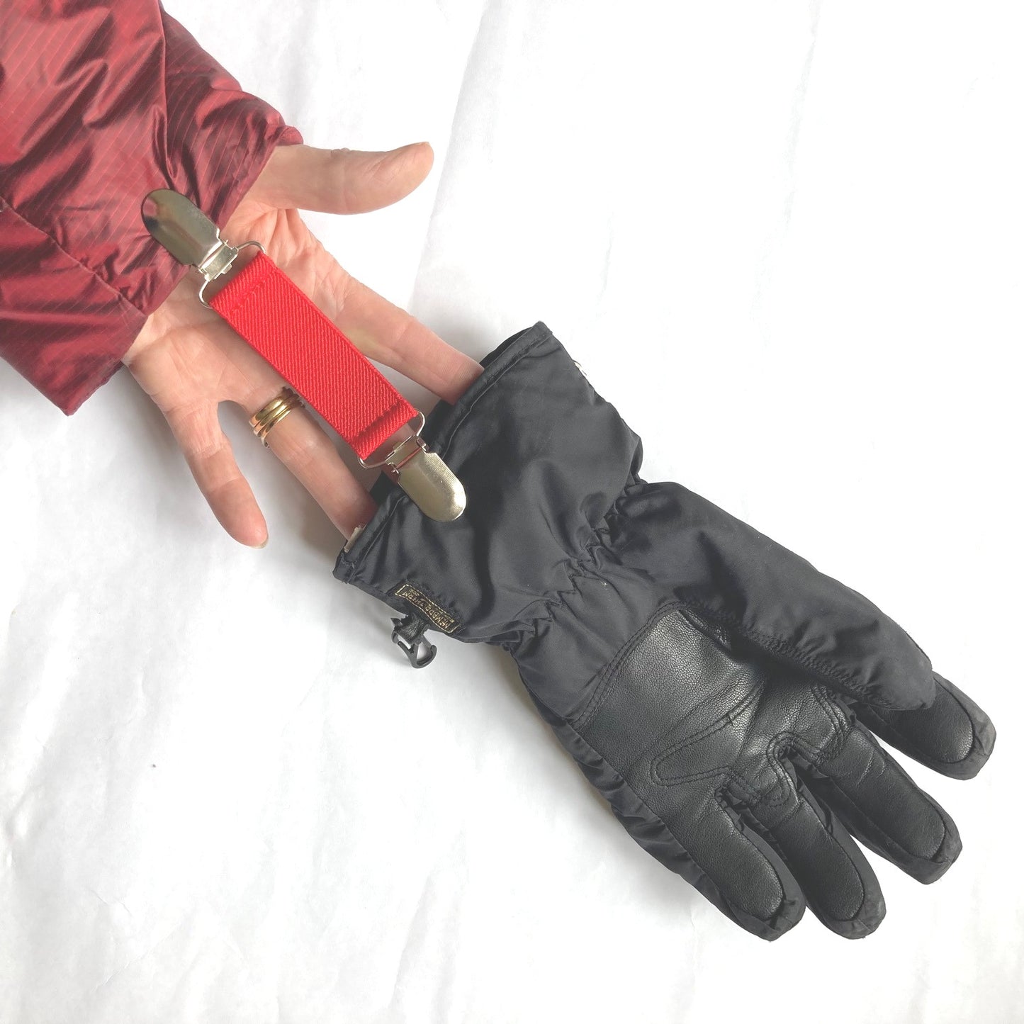 Close up of a red Clip2Cuff attached to a cuff at one end and a glove at the other end of the elastic strap