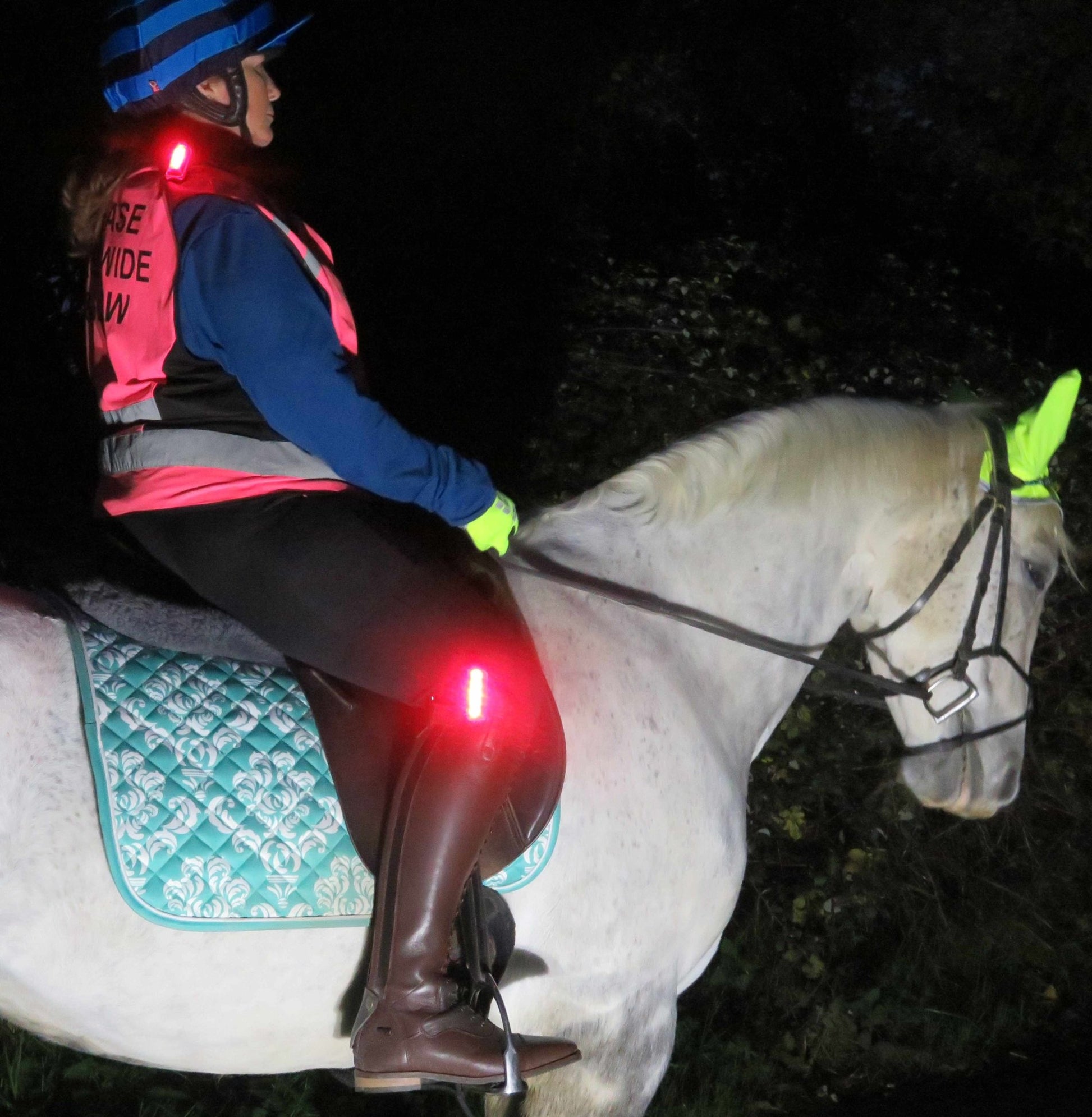 Lateral night time view of a horse and rider with trixski LED Light in use on a riding gilet and on a riding boot